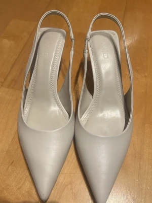 NA-KD klackar (slingbacks), strl 36 - Eleganta spetsiga klackar i ljus beige/vit. Endast använda 1 gång, i mycket fint skick. Perfekta till både vardag och fest. Nypris 499 kr.