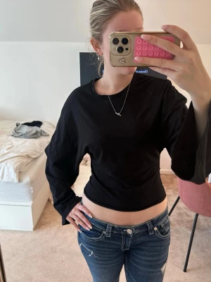 Svart croppad långärmad topp - Säljer en svart croppad topp med långa ärmar och rund hals. Toppen överdel har en loose passform och nederdelen är tajtare. Den är enkel och stilren, perfekt att matcha med jeans eller kjol. Materialet känns som bomull och är mjukt mot huden.