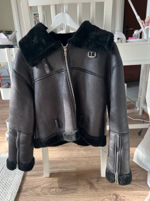 Svart pälsjacka med dragkedja - Säljer en svart pälsjacka ifrån NA-KD med bred krage och detaljer i fuskpäls. Jackan har en asymmetrisk dragkedja, spänne vid halsen och muddar i pälsimitation. Materialet är kraftigt och ger en lyxig känsla, perfekt för kalla dagar. Snygg och trendig modell som håller värmen. Jackan är i fint skick och även ett svart bälte följer med:)