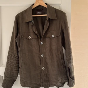 Olivgrön overshirt från Oscar Jacobson - Stilren olivgrön overshirt från Oscar Jacobson i linne. Klassisk krage, knappstängning framtill och två bröstfickor med lock och knapp. Perfekt lager på lager-plagg med avslappnad passform och diskreta sidfickor. Snygg och enkel att matcha till olika outfits. Nypris: 3000 kr, mitt pris: 1000 kr