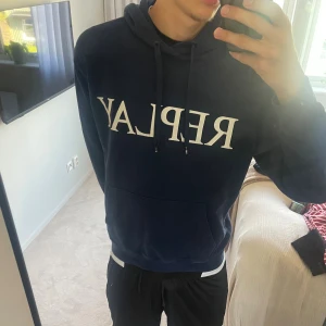 Mörkblå hoodie från Replay - Mörkblå hoodie från Replay med stor vit logga på bröstet. Klassisk känguruficka framtill, huva med snörning och mjukt bomullsmaterial. Två hål på tröjan men inget allvarligt original pris runt 1000