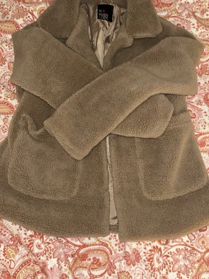 Beige teddyjacka från Even&Odd - Mysig beige teddyjacka från Even&Odd med två stora framfickor och klassisk krage. Jackan har ett mjukt, fluffigt material. Perfekt för att hålla värmen under kyliga dagar.