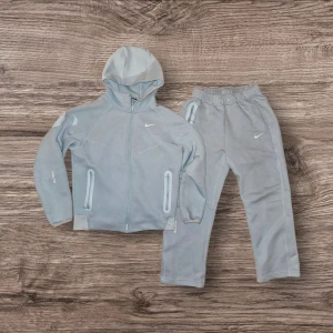Ljusblått Nike loungewear-set - Mysigt loungewear-set från Nike i ljusblått. Setet består av en hoodie med dragkedja, två fickor och Nike-logga på bröstet samt matchande byxor med resår i midjan och logga på benet. Perfekt för chill dagar hemma. Tröjan är i helt nytt skick men byxorna har några defekter, visas på bilderna