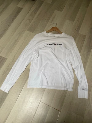 Vit långärmad t-shirt Tommy Jeans - Vit långärmad t-shirt från Tommy Jeans med logga och text på bröstet samt liten flaggdetalj på ärmen. Klassisk rund hals och relaxed fit. Perfekt till jeans eller shorts för en clean och enkel look.