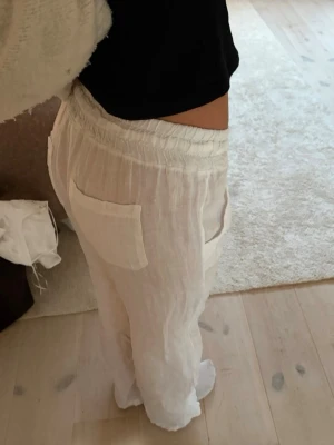 Vita linnebyxor med resårmidja - Säljer ett par vita linnebyxor med avslappnad passform och bred resår i midjan. Byxorna har raka ben och två stora fickor bak. Perfekta för en chill och luftig stil under varma dagar.