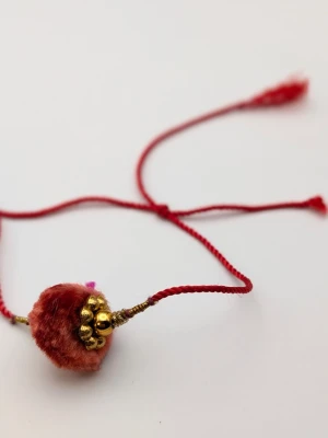 Rött armband med guldpärlor - Unikt armband med röd tvinnad tråd och en dekorativ mittdel i mjuk röd plysch. Armbandet har små guldfärgade pärlor och detaljer som ger en bohemisk och färgstark känsla. Perfekt accessoar för dig som vill sticka ut med något personligt.