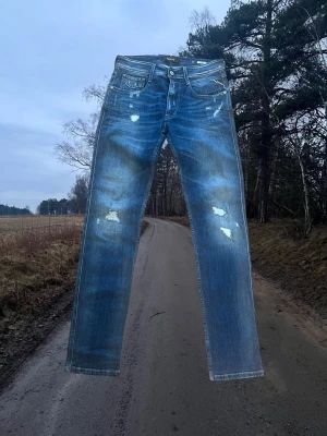Replay Anbass Slim Fit Jeans - Replay Anbass Slim Fit jeans i mycket fint skick. Endast använda ett fåtal gånger – inga fläckar eller hål. • Modell: Replay Anbass Slim Fit • Storlek: W31 L34 midja 39(platt) innerben 82 cm • Material: 98% bomull, 2% elastan (stretch) • Färg: Blå denim med slitna detaljer • Passform: Slim fit Bekväma jeans med stretch som sitter snyggt. Perfekta till både vardag och mer uppklädd stil. Skickas snabbt. Hör gärna av dig vid frågor! 