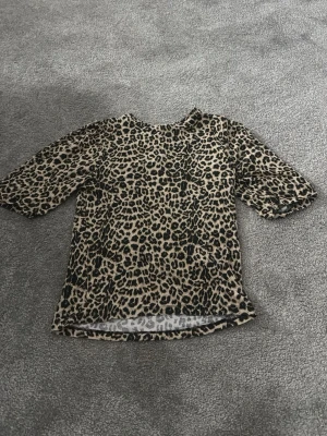 Leopardmönstrad topp med halvärm - Cool topp med leopardmönster i beige och svart. Modellen har rund hals och halvärm, perfekt för dig som vill sticka ut. Materialet känns mjukt och stretchigt, vilket gör den bekväm att bära. Passar till både jeans och kjol för en trendig look.