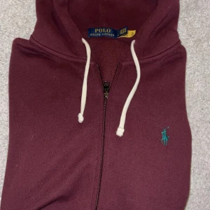 Ralph Lauren zip - Säljer en vinröd hoodie från Polo Ralph lauren. Tröjan är använd fåtal gånger och är i princip helt ny. Hoodien är beställd ifrån Ralph laurens hemsida för 2395kr               och är i storlek S. 