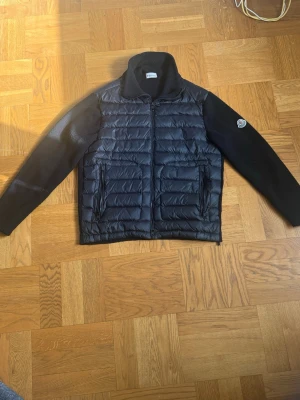 Svart cardiganjacka från Moncler (Med NFC tagg🤩 - Snygg svart cardiganjacka från Moncler med quiltad front och stickade ärmar. Jackan har två dragkedjeförsedda fickor och en hög krage. Moncler-logga på vänster ärm. Perfekt för lager-på-lager och streetwear.
