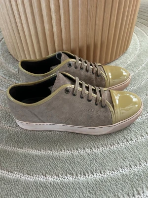 Lanvins - Stilrena sneakers i beige mocka med glansig, ljusgul lackad tå och matchande kant. Skorna har vita sulor och klassisk snörning. Perfekta för dig som vill ha en unik twist på vardagslooken.