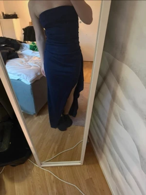 Mörkblå axelbandslös långklänning - Snygg mörkblå axelbandslös långklänning med slits på sidan. Klänningen har en figurnära passform och är perfekt för dig som vill ha en stilren och elegant look. Materialet är stretchigt och följsamt.