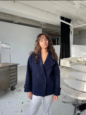 Marinblå skepparkavaj med dubbelknäppning - Säljer en marinblå kappa med bred krage och dubbelknäppning. Perfekt nu till våren! Den har en liten slitning i fodret i ryggen, men ingenting som stör eller syns (se sista bilden) 