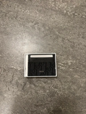 korthållare i canvas - Snygg svart korthållare  med diskret logomönster och detaljer i läder. Praktisk och stilren design med flera kortfack, perfekt för dig som vill ha ett lyxigt och smidigt alternativ till plånbok. Kommer i original ask.