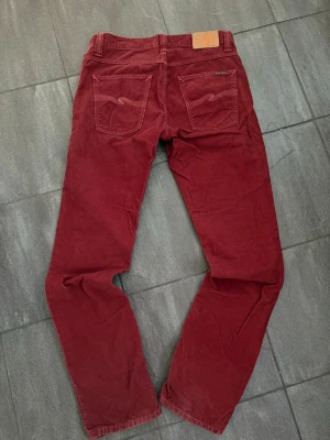 Vinröda manchesterbyxor från Nudie Jeans - Snygga vinröda manchesterbyxor från Nudie Jeans med klassiska bakfickor och logga på läderpatch baktill. Cool design och rak passform perfekt för sommarn 