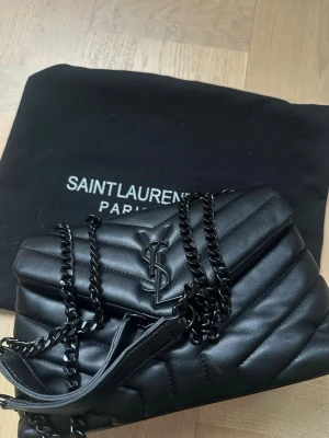 Svart YSL väska  - Jättefin svart väska från Saint Laurent i modellen Loulou och stoleken Small. Väskan har en kedja och magnet lås och är tillverkad i läder. Det medkommer dustbag men dessvärre inget kvitto då jag tappat bort det, därav priset. Priset kan diskuteras.