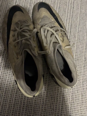 Nike Mercurial fotbollsskor beige/svart - Säljer ett par Nike Mercurial fotbollsskor i beige med svarta detaljer. Skorna har snörning, låg profil och är tillverkade i syntetmaterial för bra grepp och känsla på planen. Perfekta för dig som vill ha lätta och smidiga skor till match eller träning.