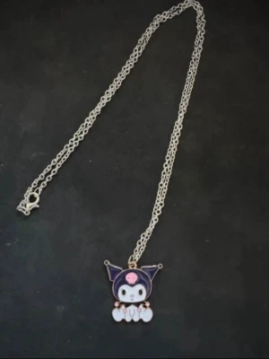 Silverfärgat halsband med Kuromi-berlock - Snyggt halsband med en silverfärgad kedja och en berlock föreställande Kuromi från Sanrio. Berlocken är i svart, vitt och rosa och har en söt, tecknad design. Perfekt accessoar för dig som gillar kawaii-stil och unika smycken.