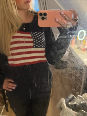 Mörkblå stickad tröja Playback - Säljer en mörkblå stickad tröja från Playback med amerikansk flagga i rött, vitt och blått på bröstet. Tröjan har rund halsringning och långa ärmar. Perfekt för dig som gillar klassisk college-stil 