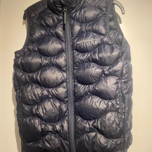Peak Perfomance DunVäst Navy Blue - En riktigt skön peak performance väst som funkar både till kalla och varma dagar! Skicket är Bra och det finns bara ett litet hål som inte märks av (det kommer inte ut nått dun genom det). Passar perfekt och du är mellan 160 och 170! Hör av er vid eventuell frågor eller funderingar.