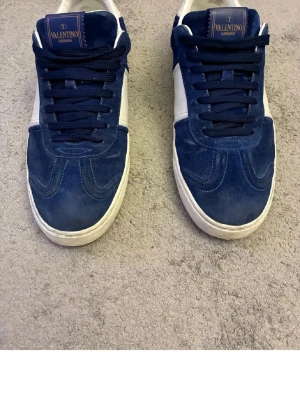 Valentino flycrew skor - Snygga sneakers från Valentino Garavani i blå mocka med vita detaljer och vit sula. Klassisk låg modell med blåa skosnören och logotyp på plösen. Perfekta för dig som vill ha en stilren och exklusiv look.