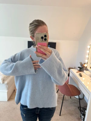 Ljusblå oversized stickad tröja - Mysig ljusblå stickad tröja med breda ribbade muddar och avslappnad passform. Tröjan har rund halsringning och långa ärmar med extra långa muddar. Perfekt för att skapa en chill och trendig look.