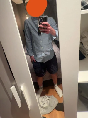 Blå skjorta från Polo Ralph Lauren - Säljer en klassisk ljusblå skjorta från Polo Ralph Lauren med broderad logga på bröstet. Skjortan har knappar framtill, långärmad design och är tillverkad i bomull. Perfekt för dig som vill ha en stilren och tidlös look.