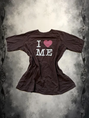 Brun t-shirt med I ❤️ ME-tryck - Brun t-shirt med vit text och ett rosa hjärta på bröstet där det står 'I ❤️ ME'. Klassisk rund halsringning och korta ärmar. Tillverkad i mjuk bomull för en skön känsla. Perfekt för dig som vill sprida självkärlek med stil.