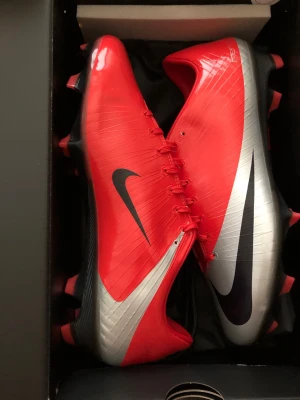 Nike Mercurial CR7 fotbollsskor röd/silver - Snygga Nike Mercurial CR7 fotbollsskor i rött och silver med svarta detaljer. Skorna har en smal, aerodynamisk form och stora Nike-loggor på sidorna. Helt nya!
