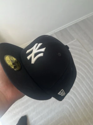  New Era Yankees keps - Snygg svart keps från New Era med New York Yankees-logga broderad i vitt framtill. Klassisk flat brim och MLB-logga baktill. Kepsen är i ett stadigt material och har en ikonisk streetstyle-look använd bara en gång 