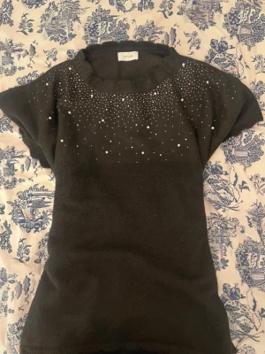 Svart stickad topp med pärlor från Vila - Elegant och feminin modell med mjuk stickad kvalitet och fina detaljer framtill som gör toppen extra speciell. Perfekt både till vardag och festligare tillfällen. Superfin till jeans, kjol eller skinnbyxor för en classy och chic look🖤