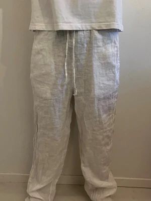 Vita linnebyxor från Chelsea - Säljer ett par vita linnebyxor med avslappnad passform och elastisk midja med dragsko. Byxorna är tillverkade i svalt och luftigt linne, perfekta för varma dagar. Klassisk rak modell utan synliga fickor eller detaljer.