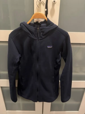 Patagonia fleece hoodie - Marinblå fleece hoodie från patagonia i storlek M. Den är knappt använd och i mycket bra skick. Skulle säga att den är mer åt M/S hållet 