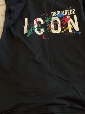 Svart Dsquared2 ICON t-shirt - Cool svart t-shirt från Dsquared2 med stort vitt 'ICON'-tryck på bröstet och färgglada stänk i grönt, blått, rött och gult. Materialet är mjukt och bekvämt, perfekt för dig som gillar streetstyle och grafiska prints.