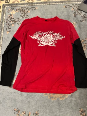 Röd långärmad topp med tryck - Cool röd topp med svartvita långa ärmar och ett stort vitt tryck framtill med text och grafiskt mönster. T-shirten har en rund halsringning och är gjord i mjukt bomullsmaterial. Perfekt för en avslappnad streetstil.