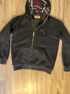 Burrberry hoodie svart - Svart burrberry hoodie med vit/röd rutigt mönster i luvan och en hästlogga på vänstra bröstet