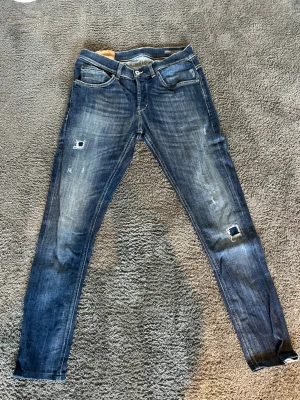 Dondup george jeans - Snygga mörkblå skinny jeans med slitningar och hål på knäna. Jeansen har klassisk femficksdesign, låg midja och lätt tvättade detaljer framtill och baktill. Perfekta för en avslappnad och trendig look.