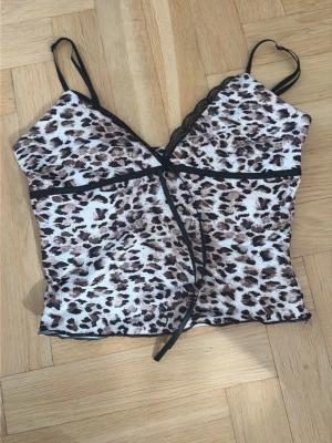 Leopardmönstrad body med spets - Säljer en leopardmönstrad body med tunna axelband och svarta spetsdetaljer längs urringningen. Bodyn har en figurnära passform och är tillverkad i ett stretchigt material som känns mjukt mot huden. Perfekt för dig som gillar djurmönstrat och vill ha något extra.