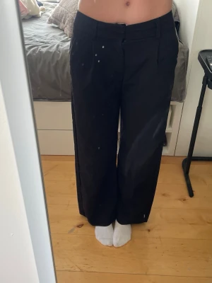 Svarta vida kostymbyxor - Säljer ett par svarta kostymbyxor med rak och vid passform. Byxorna har hällor för skärp och klassisk stängning fram. Perfekta för en stilren look och passar till många olika outfits.