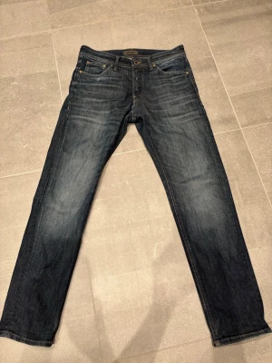 Mörkblå raka jeans från Jack & Jones - Snygga mörkblå jeans från Jack&Jones med klassisk rak passform och fem fickor. Jeansen har subtila slitningar och kontrastsömmar, samt en läderpatch bak i midjan. Perfekta för en avslappnad och stilren look.
