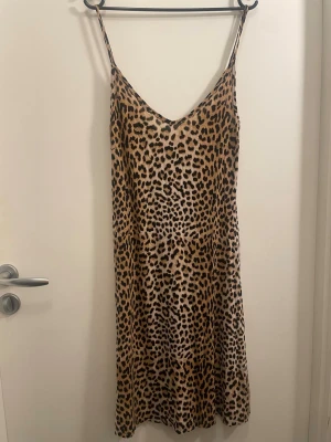 Leopardmönstrad klänning Gina Tricot - Säljer en leopardmönstrad klänning från Gina Tricot med tunna axelband och v-ringning. Klänningen har en loose passform och är tillverkad i ett mjukt, lätt material som känns skönt mot huden. Perfekt för dig som vill sticka ut med ett djurmönster.