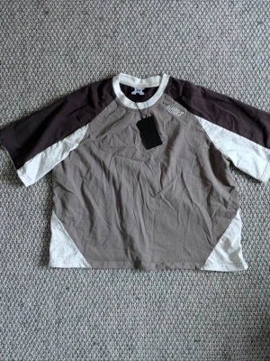 Ny cropped Mertra T-shirt Size S - Helt ny Mertra T-shirt grey/black med tags kvar. Oversized cropped fit med raglanärmar i kontrastvitt. Grym kvalitet i 100% bomull och snyggt broderad logga i deras signatur grungefont på ryggen. Perfekt för dig som vill ha något unikt att sticka ut ifrån mängden ;)