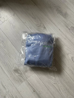 Ljusblå Deftones hoodie med orm - Snygg ljusblå hoodie med huva från Deftones. Framsidan har Deftones-logga och texten SACTO, CA i vitt och grönt. Baksidan pryds av en stor vit orm och grön Deftones-text. Klassisk känguruficka och mjukt material, perfekt för dig som gillar bandmerch. ALDRIG ANVÄND
