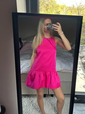 Rosa ärmlös kortklänning - Säljer en söt rosa kortklänning med volang nertill. Klänningen är ärmlös och har en enkel, rak passform som ger en avslappnad men ändå trendig look. Perfekt för varma dagar och sommarens alla tillfällen.
