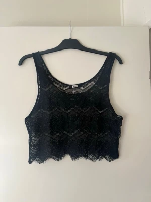Svart spetsig croppad linnetopp - Snygg svart croppad linnetopp från Bik Bok i genombruten spets med blommigt mönster. Toppen är ärmlös och har en rund halsringning. Perfekt att styla med höga jeans eller kjol för en trendig look.