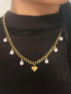 Guldigt halsband 6 mm brett med hjärthänge - Matchande örhängen finns i en separat annons. Finns även i rostfri variant.  Material: 14K guldplätering på rostfritt stål Bredd: 6 mm Längd: 42 + 8 cm (justerbar) Övrigt: Nickeltestad och handgjort Märke: Diavansa smycken