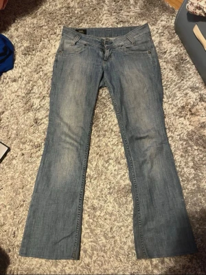 Ljusblå bootcut jeans från Lee - Snygga ljusblå bootcut jeans från Lee med klassisk femficksdesign och diskreta slitningar framtill. Jeansen har normal midja och Lee-logga på bakfickan. Perfekta för en avslappnad och trendig look.