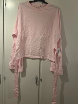 Ljusrosa långärmad topp från Nelly - Ljusrosa långärmad topp från Nelly i mjuk bomull. Modellen har rund halsringning, långa ärmar och knytband i sidorna för en cool detalj. Perfekt att styla med jeans eller kjol för en trendig look.