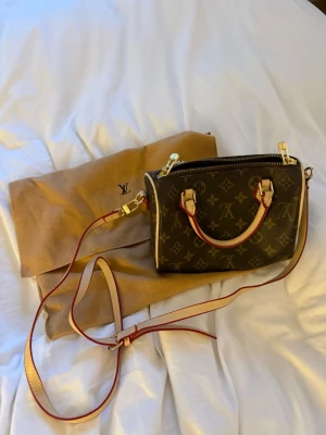 handväska - Snygg handväska i klassiskt brunt monogrammönster med beige och röda detaljer. Väskan har guldfärgade metalldetaljer, dragkedja och två handtag. 