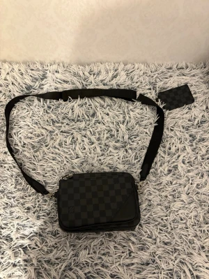 Louis Vuitton axelväska Damier Graphite - Snygg axelväska från Louis Vuitton i klassiskt Damier Graphite-mönster. Väskan är svart och grå med justerbar axelrem och matchande korthållare. Tillverkad i slitstarkt skinn med rutigt mönster och dragkedja upptill. Äkta!!